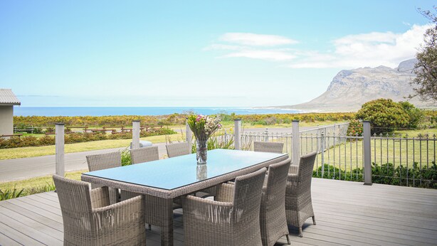 Een terras met rieten meubilair en een glazen tafel, met uitzicht op een kustlandschap met een berg in de verte.