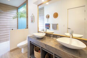 A modern bathroom with two sinks, a toilet, and a shower.