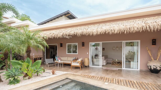 Et moderne hus med swimmingpool, udendørs møbler og tropiske planter.