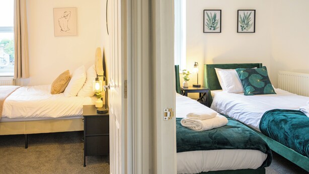 A hotel room with two beds, a nightstand with a lamp, and artwork on the walls.