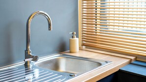 A modern bathroom with a chrome faucet, a wooden countertop, and a window with blinds.