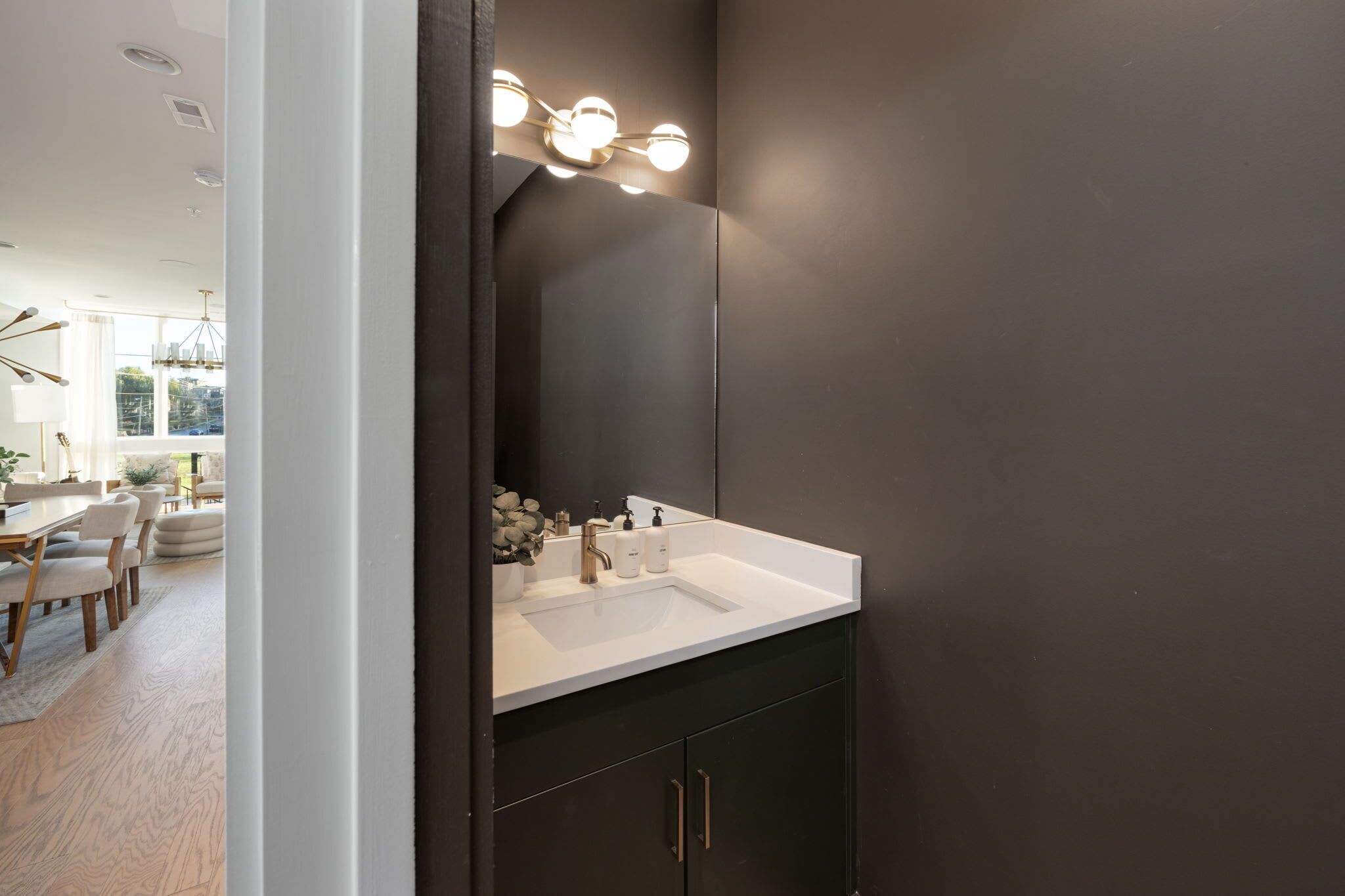 Un baño moderno con una pared oscura, un lavamanos blanco y un espejo con iluminación.