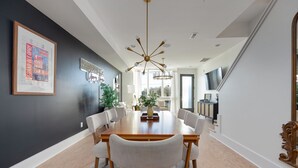 A dining area with a long wooden table, white upholstered chairs, and a modern chandelier.
