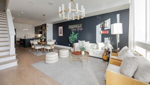 A modern living room with a staircase, a dining area, and a kitchen in the background.