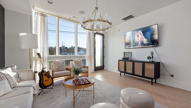 A modern living room with a large window, a chandelier, a television, and a guitar.