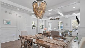 A spacious dining area with a wooden table and chairs, a decorative chandelier, and a ceiling fan. - Pearl House: Luxury Retreat with Bikes and Golf Cart, and Pond & Nature Views, Pickleball Courts! (Santa Rosa Beach)