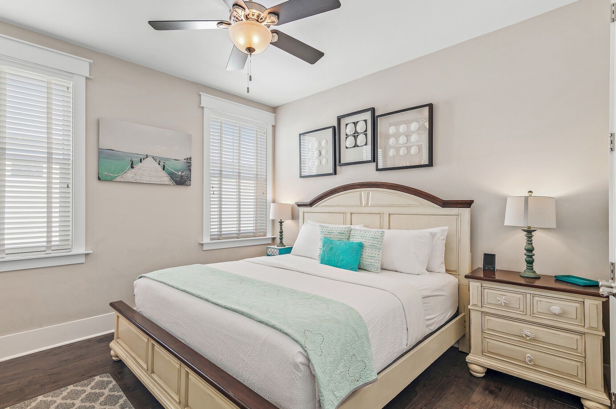 A bedroom with a bed, a nightstand, a lamp, a ceiling fan, and framed pictures on the wall.