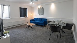 A modern living room with a blue sofa, a glass coffee table, and a dining table set for four. - 2-bedroom- Stoke-on-trent-sleeps 5-petsok (Stoke-on-Trent)
