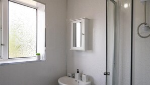 A bathroom with a white sink, a medicine cabinet, a window with a plant, and a glass shower enclosure. - 2-bedroom- Stoke-on-trent-sleeps 5-petsok (Stoke-on-Trent)
