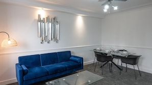 A modern living room with a blue sofa, a glass coffee table, a dining area with a glass table and black chairs, and a ceiling fan. - 2-bedroom- Stoke-on-trent-sleeps 5-petsok (Stoke-on-Trent)