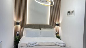 Et moderne soveværelse med en stor seng, en usædvanlig rund lampe og lodrette trælameller på væggene.