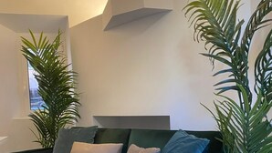 En grøn sofa med mange puder, en potteplante og en moderne aircondition.