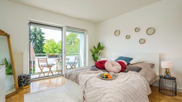 Une chambre à coucher avec un lit, une fenêtre, une plante et une petite table sur laquelle se trouve un plateau.