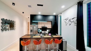 A modern kitchen with dark cabinets, a central island with bar stools, and a decorative wall art piece. - 3 Mi to Dtwn: Modern Townhome w/ Yard in Houston (Houston)