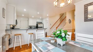Una cocina moderna con armarios blancos, una escalera de madera y una zona de comedor con una mesa y taburetes de bar.