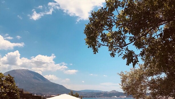 Área de piscina com espreguiçadeiras e guarda-sóis, com vista para um corpo de água e montanhas.