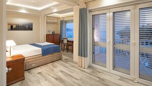 Quarto de hotel com cama, escrivaninha, cadeira, armário e uma janela grande com persianas.