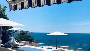 Uma área de piscina no terraço com hidromassagem, espreguiçadeiras e guarda-sóis.