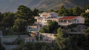 Um edifício residencial de vários andares com varandas, rodeado por vegetação densa e montanhas ao fundo.