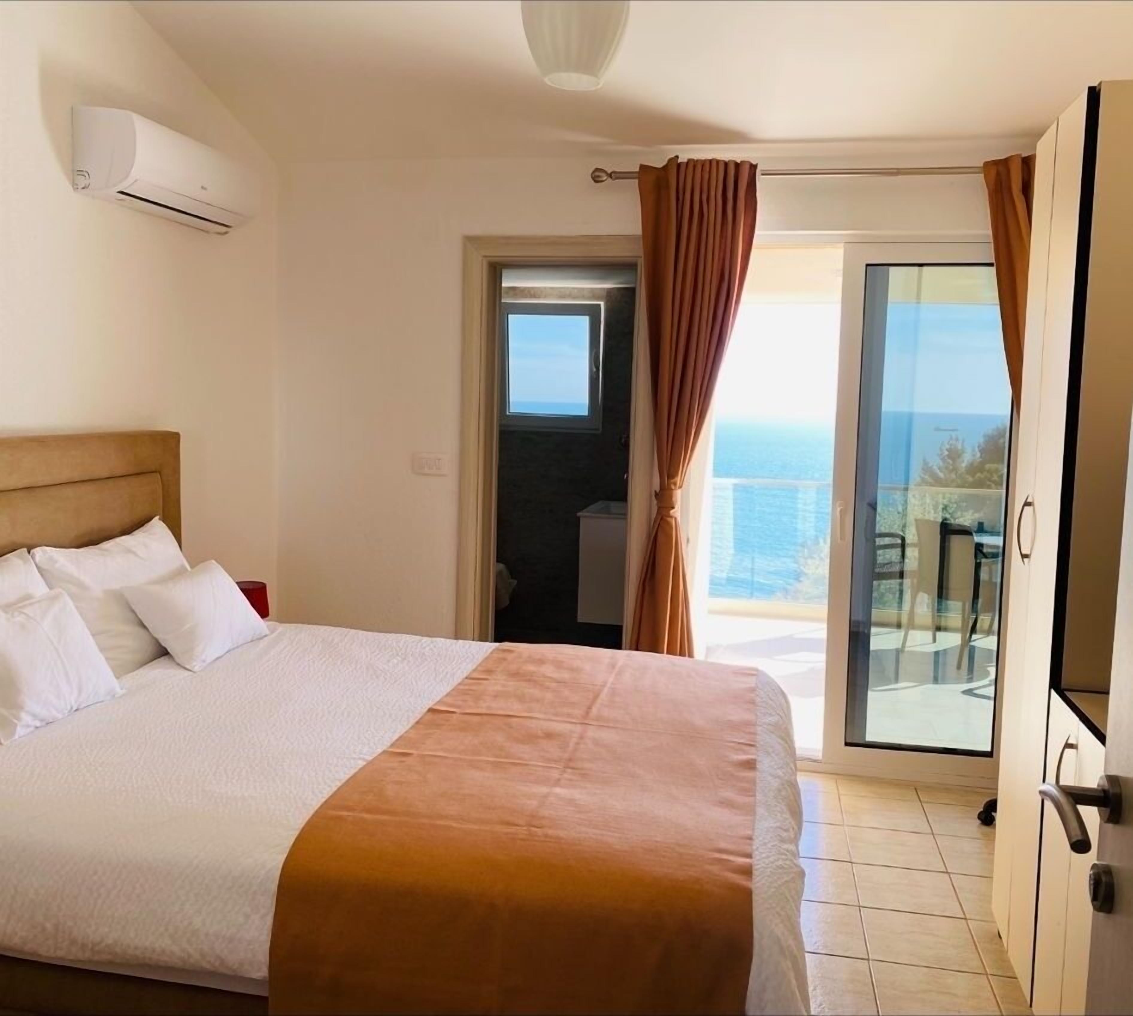 A bedroom with a bed, a window, and a view of the sea.