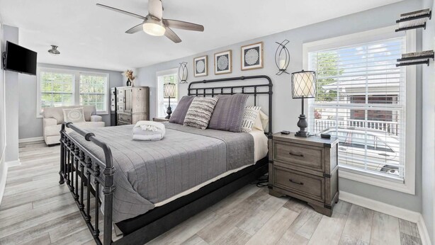 A bedroom with a bed, bedside tables, a ceiling fan, and a window with blinds. - Seashell Retreat 3/2 By Beach Star (Murrells Inlet)