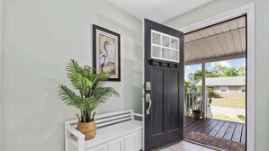 A dark door with a white window, a bench with a plant, and a view of a house through the door. - Seashell Retreat 3/2 By Beach Star (Murrells Inlet)