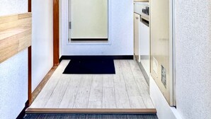 A narrow hallway with a wooden door, a black mat at the entrance, and a refrigerator on the right. - Along the airport line and 2 minutes from the nearest station, Japanese-style rooms with private bathrooms have excellent access [ 201]. (大阪市西成区花園北)