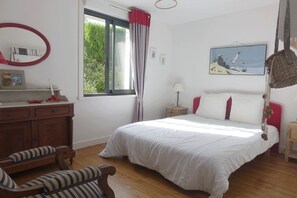 Relax in this serene bedroom with a large bed, nightstand, and comfortable chair, offering a view of lush greenery.