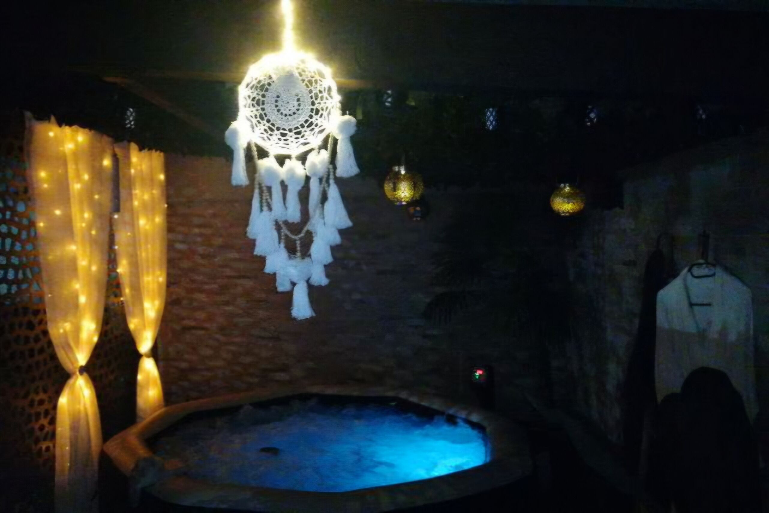 Een zwak verlichte kamer met een stenen muur, een hangende droomvanger en een klein zwembad.
