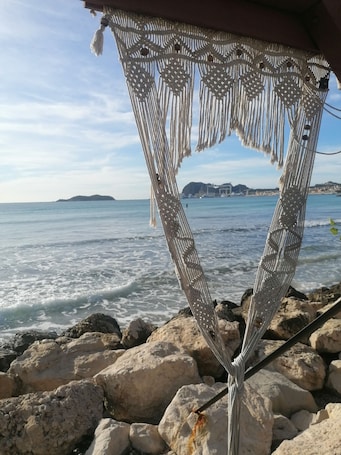 A macrame beach umbrella with a view of the sea and distant land.. Private guest room with patio and spa in Provence