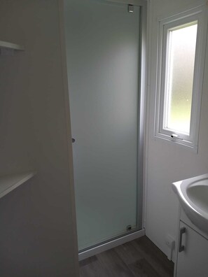 Bathroom features a glass shower door, a single window, a white sink, and a mirror.