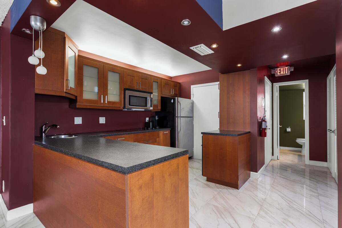 A modern kitchen with wooden cabinets, a central island, stainless steel appliances, and a marble floor.