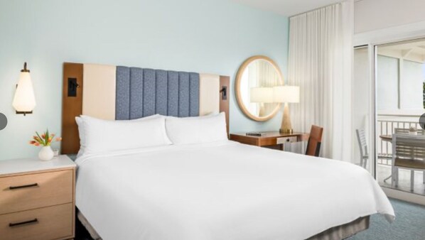 Habitación de hotel con una cama grande, un escritorio con silla, un espejo redondo y una ventana con cortinas.