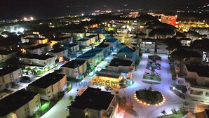 Vista aérea nocturna de una zona residencial con edificios, calles y un parque circular iluminado.