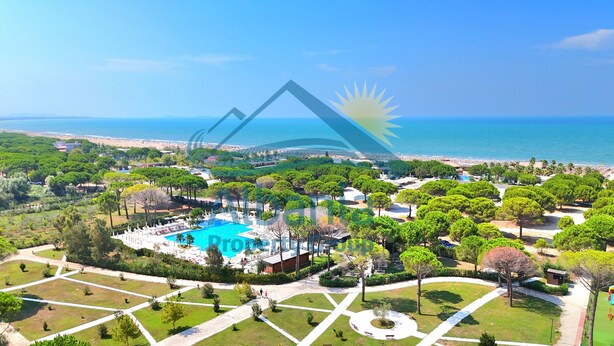 Vista aérea de un resort con una piscina central, jardines ajardinados y una playa al fondo.