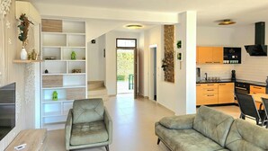 Una sala de estar moderna con un sofá, un sillón y un televisor. Cuenta con una zona de cocina con armarios y una estufa.