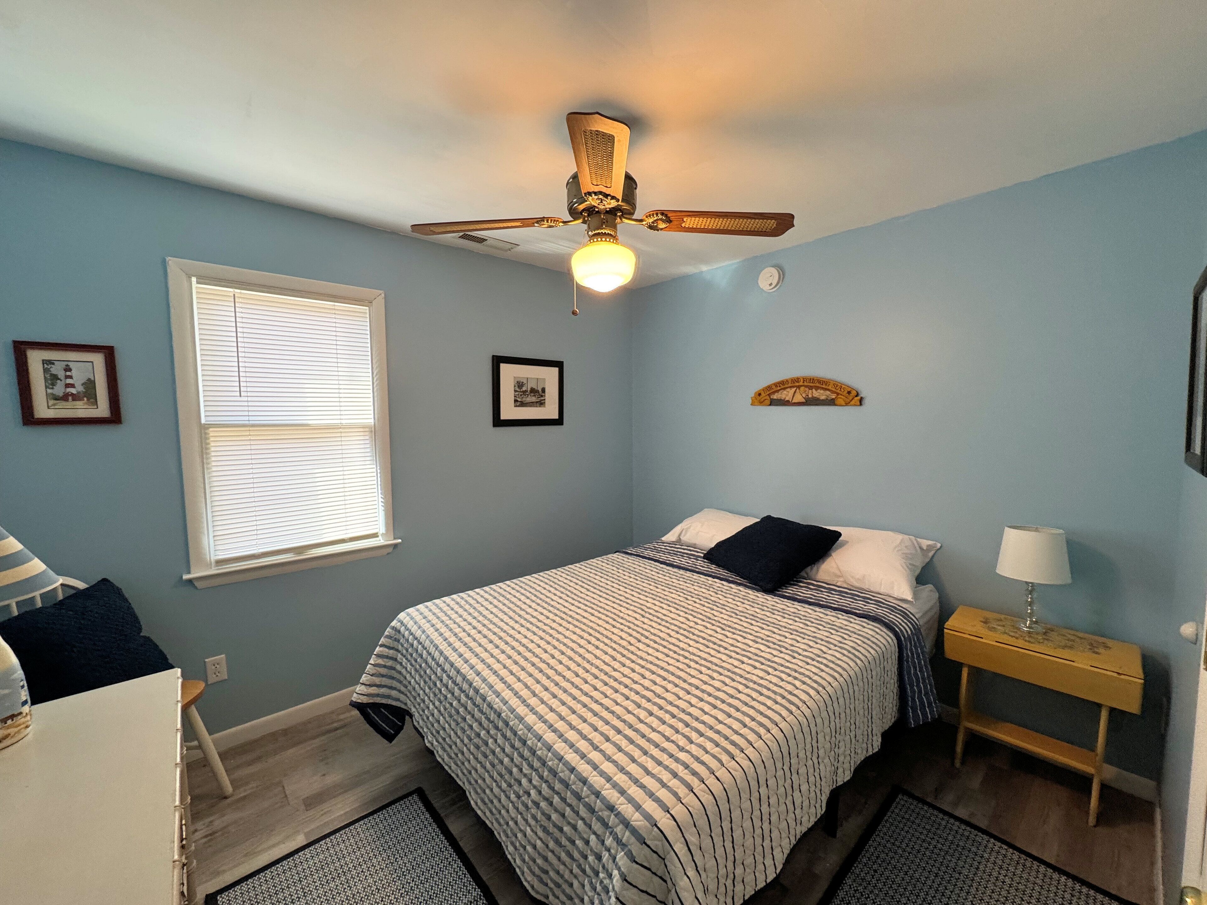 A bedroom with a bed, a ceiling fan, a nightstand, a lamp, and a window with blinds.
