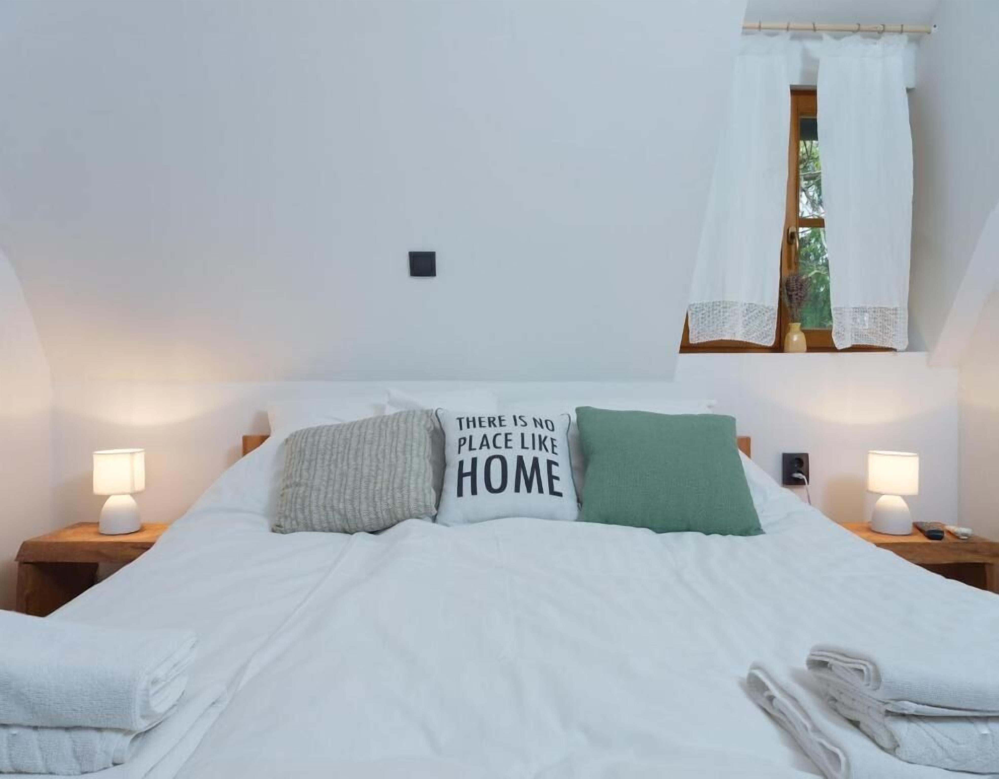 Ett sovrum med en säng, två sänglampor, ett fönster med gardin och en kudde med text på.