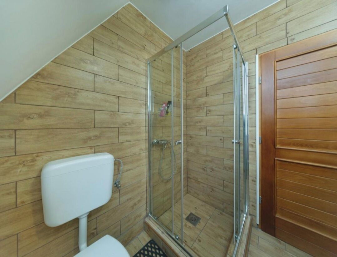 Ducha con puertas de vidrio, inodoro y paneles de madera en las paredes.