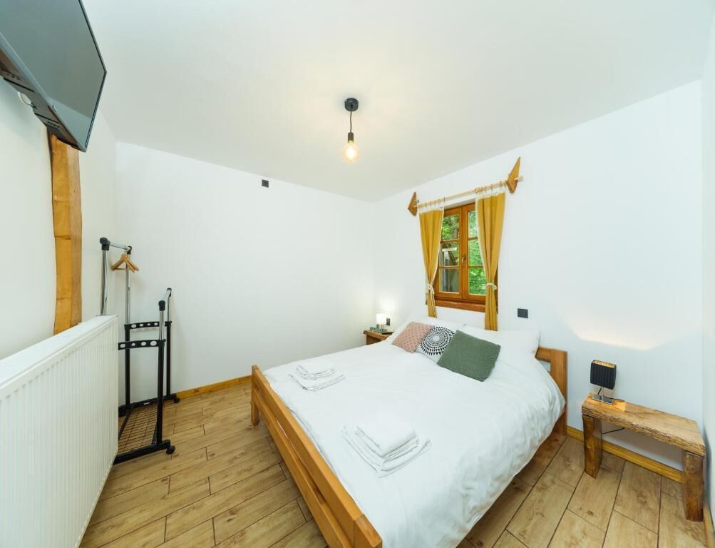 Ein Schlafzimmer mit einem hölzernen Bett, einem Fenster mit Vorhängen, einem Nachttisch und einer Heizung.