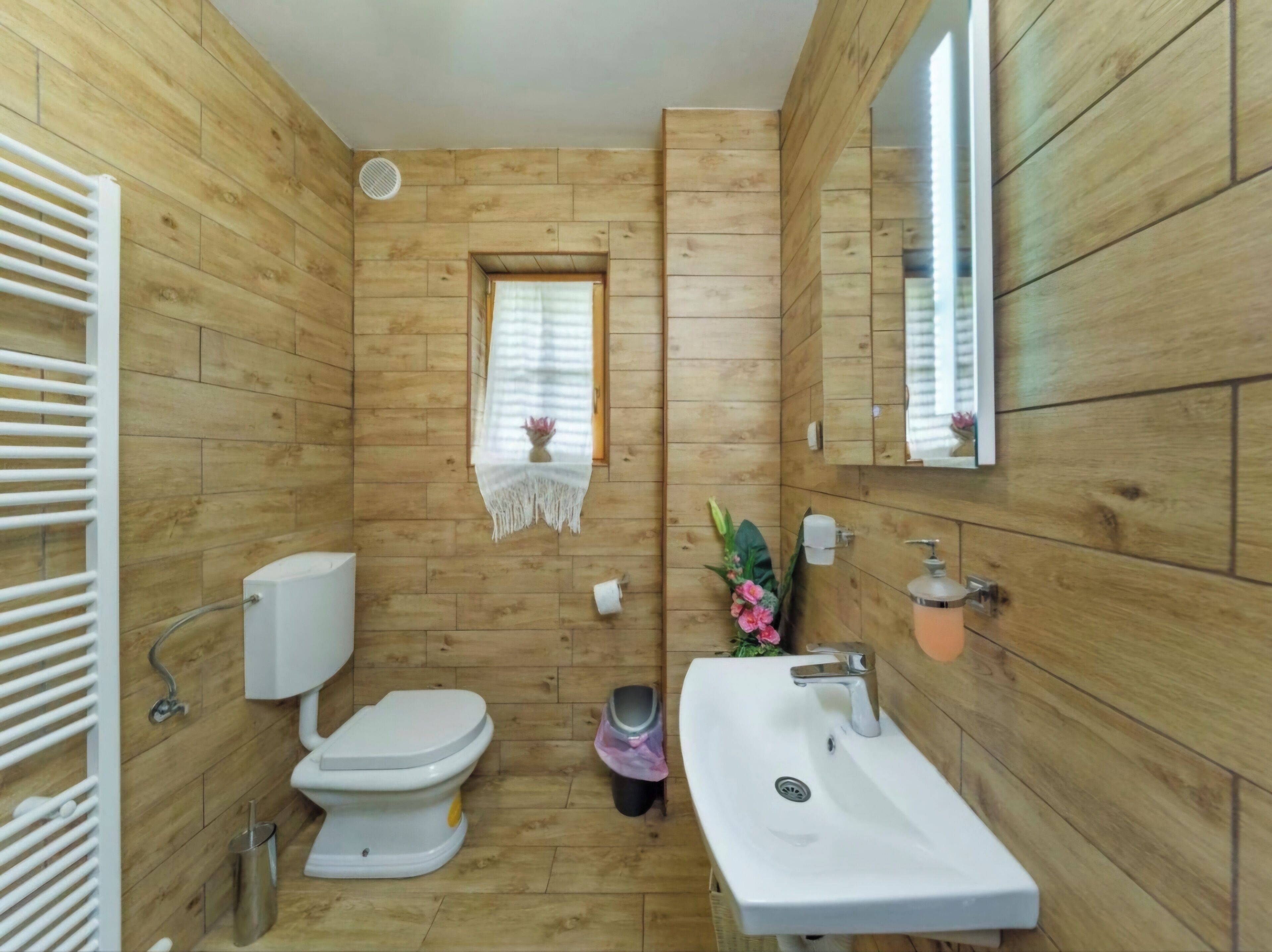 A bathroom with wooden panel walls, a toilet, a sink, and a window with a decorative item.