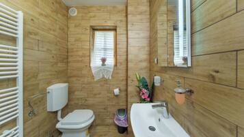 A bathroom with wooden panel walls, a toilet, a sink, and a window with a decorative item.
