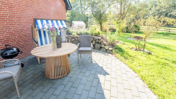 A patio with a round wooden table and chairs, a grill, and a striped awning. - Vogelkoje Living in nature, vacation apartment with terrace and beach chair (Rodenäs)