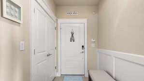 Un pasillo con una puerta blanca que dice 'BEACH HOUSE', un interruptor de luz, un termostato y una alfombra pequeña en el suelo.