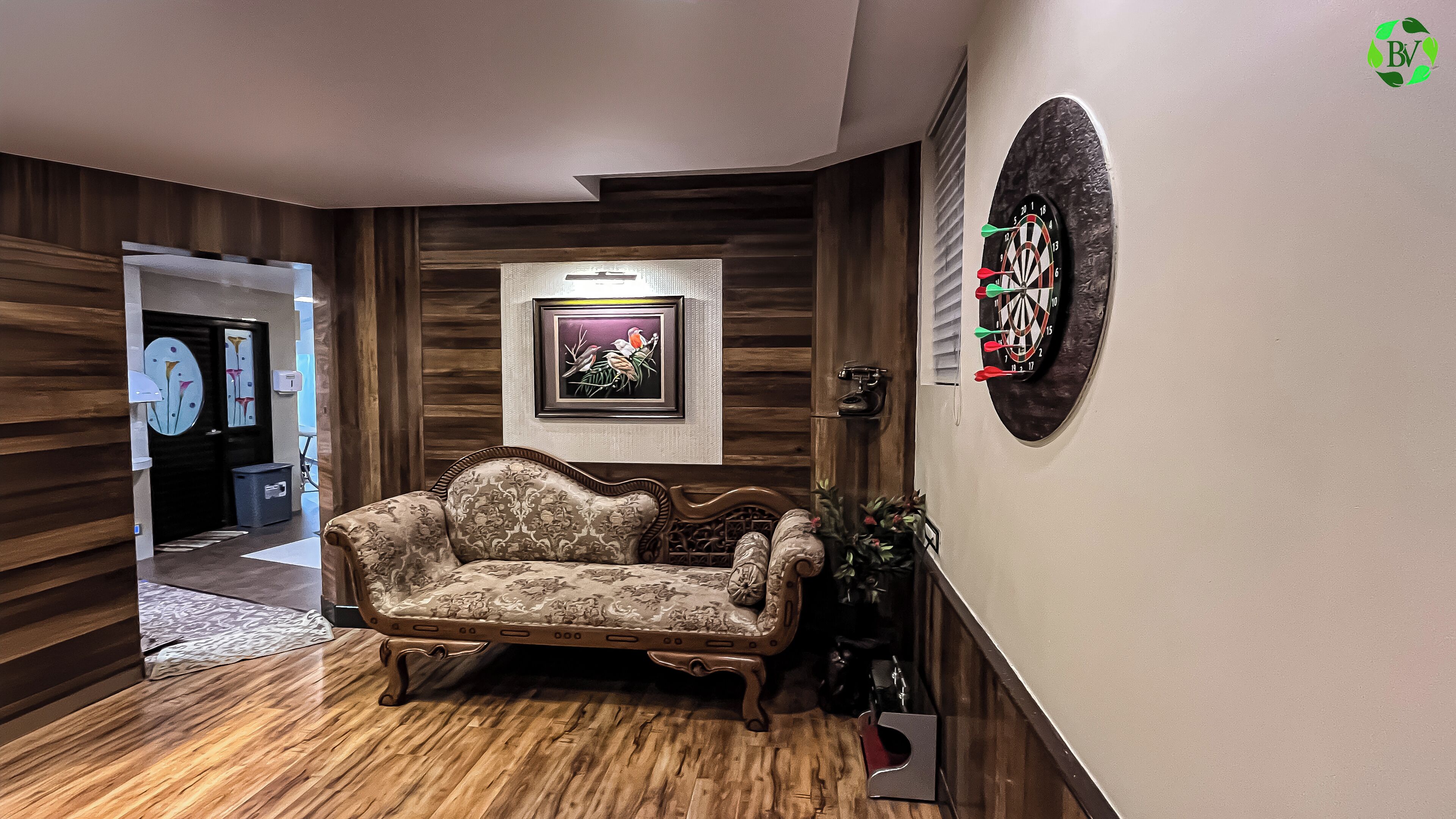 A hallway with a patterned wooden floor, a vintage sofa, a framed artwork, and a dartboard.