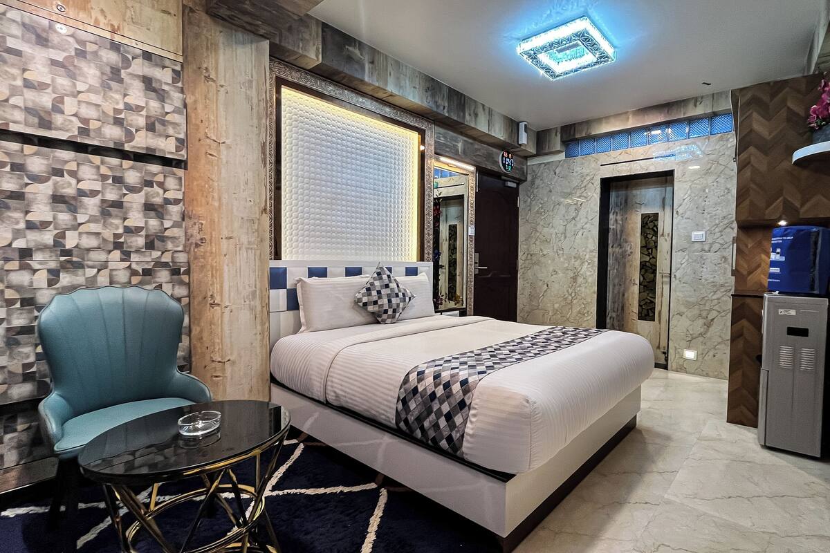 A modern hotel room with a bed, a chair, a table, a mirror, and a wardrobe.