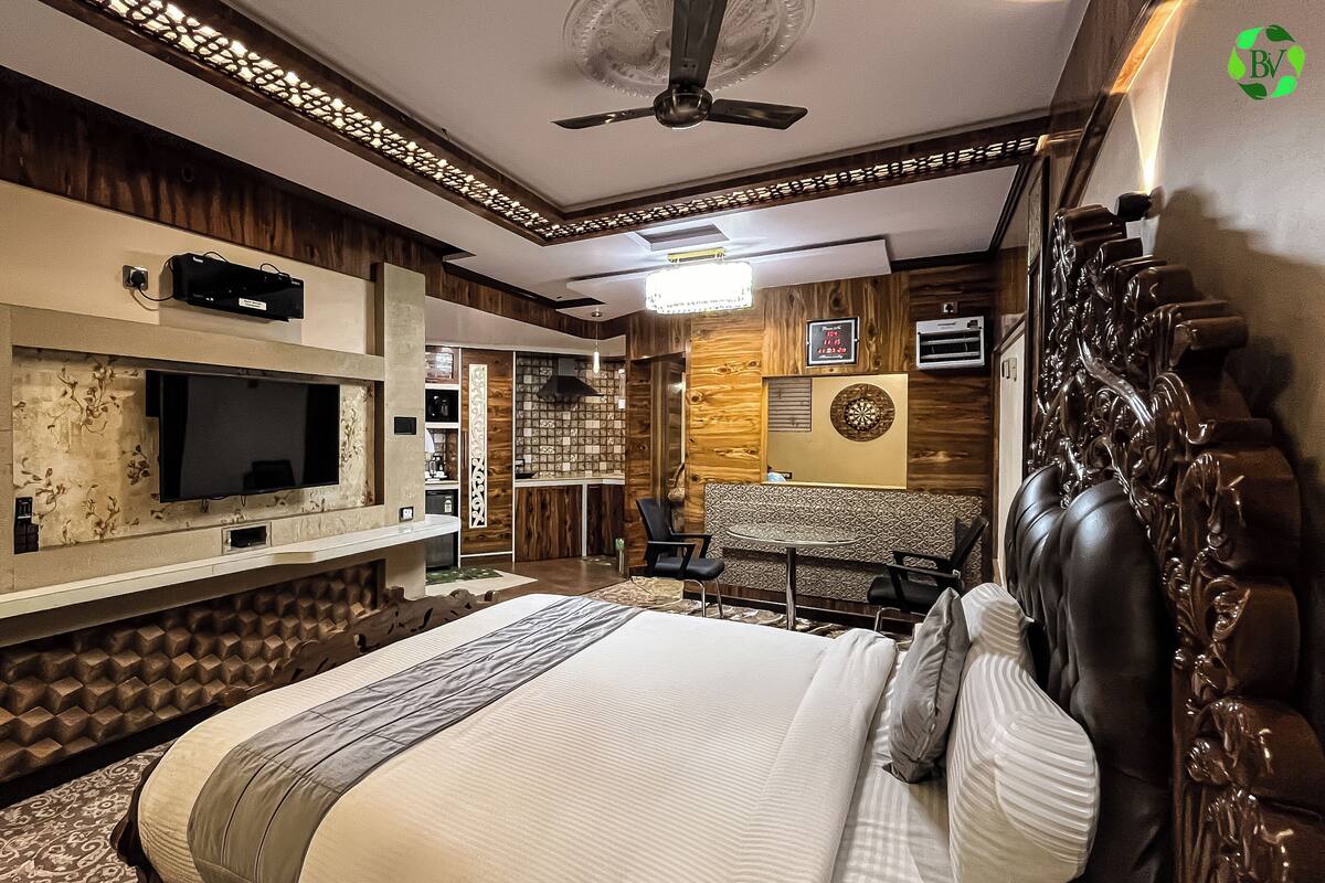 A hotel room with a large bed, a TV mounted on the wall, a ceiling fan, and a decorative wall panel.