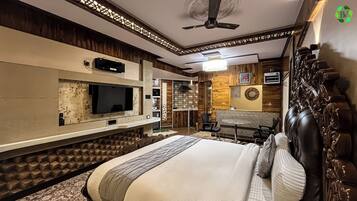 Habitación de hotel con una cama grande, televisión montada en la pared, ventilador de techo y un panel decorativo.