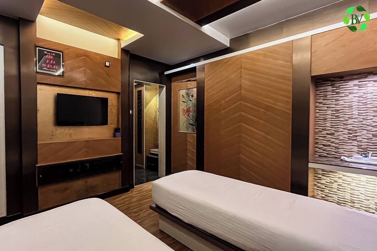 A hotel room with two beds, a flat-screen TV mounted on the wall, a digital clock, and a mirror.