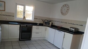 Une cuisine avec des meubles blancs, un plan de travail noir, un four à micro-ondes, un grille-pain et une horloge murale.